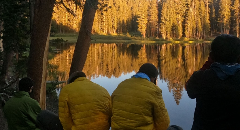 a group of people rest beside a body of water reflecting the trees